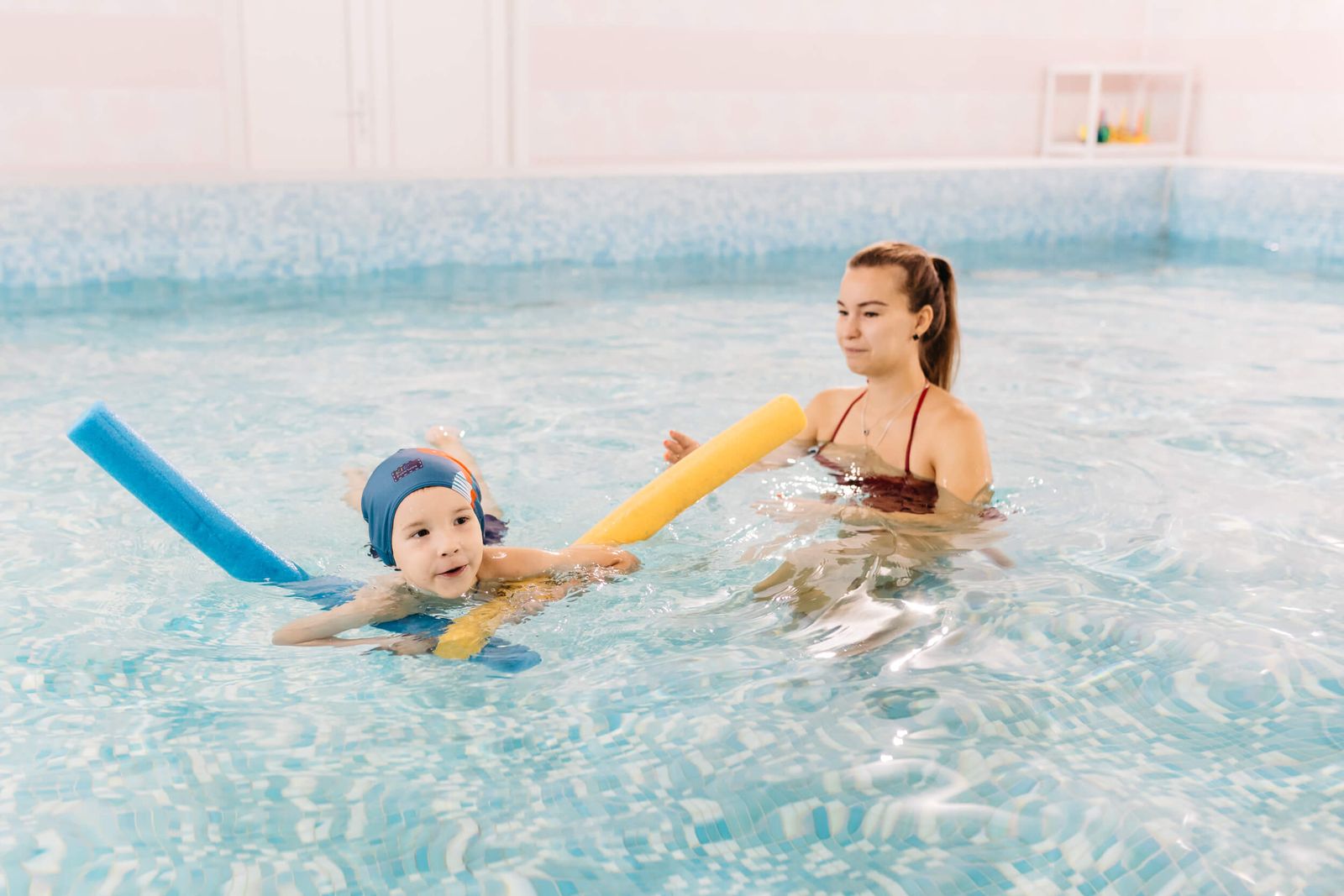 Малыш с тренером учится плавать с нудлами